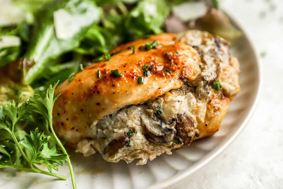 a mushroom stuffed chicken breast on a white plate with salad.