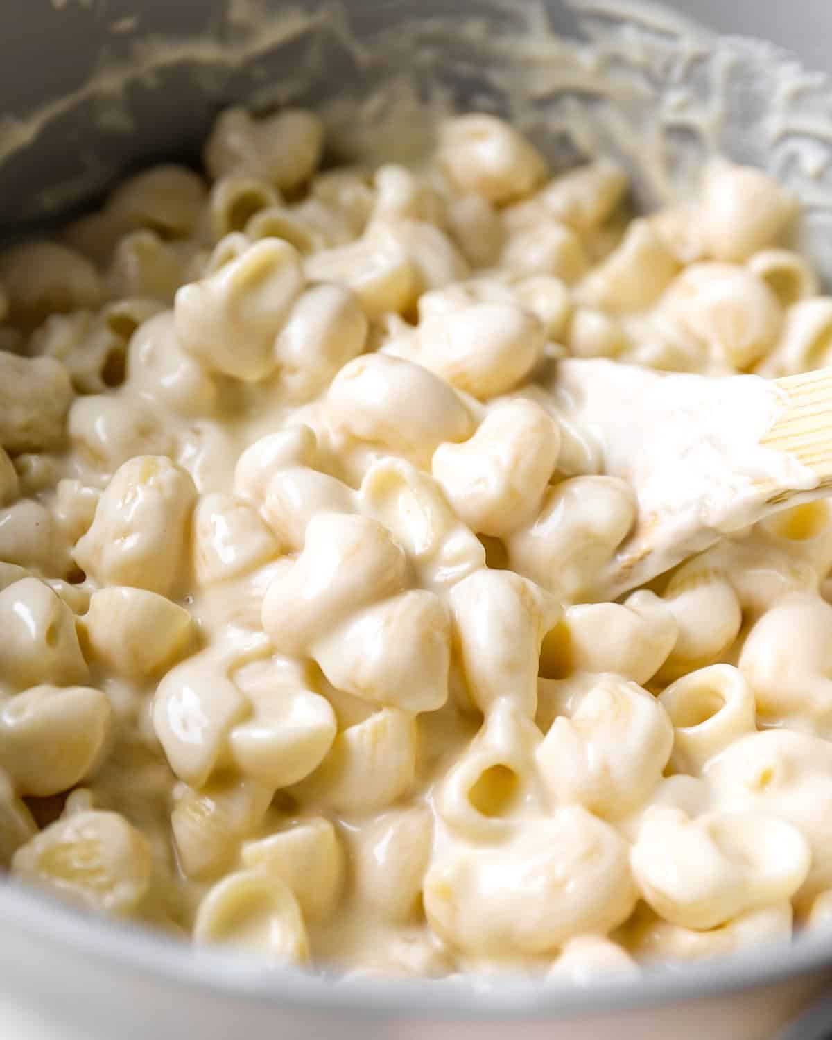 stirring creamy mac and cheese in a pot with a wooden spoon.