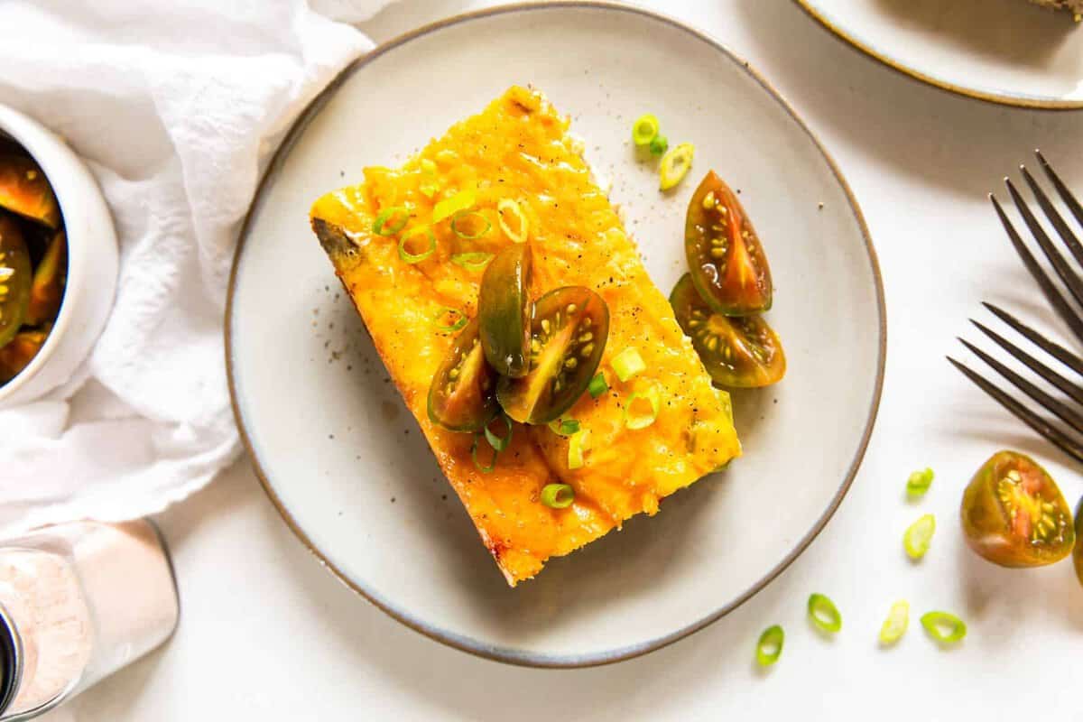 piece of sausage breakfast casserole topped with fresh tomatoes on a white plate