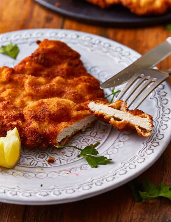 cut pork schnitzel on a plate with a fork and knife.