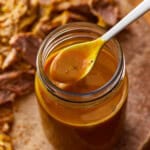 a spoon lifting carolina gold sauce from a mason jar.