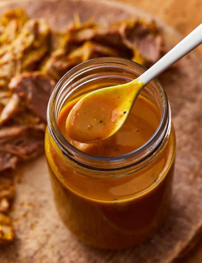 a spoon lifting carolina gold sauce from a mason jar.