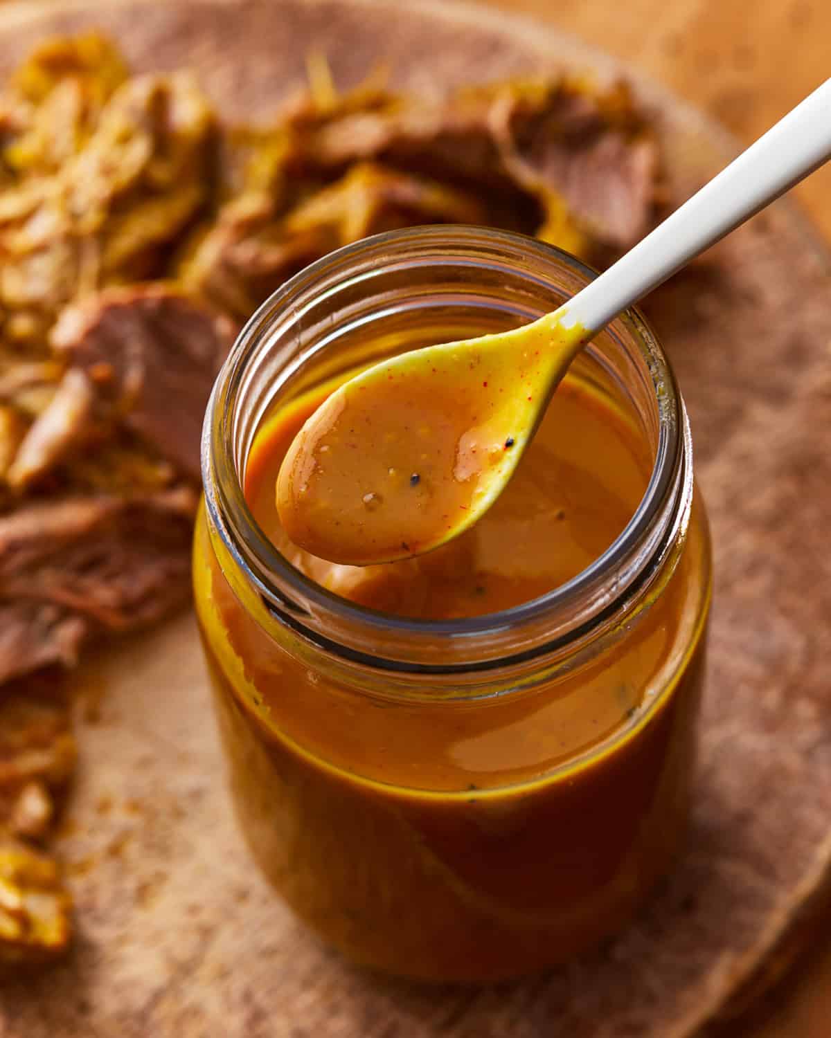 a spoon lifting carolina gold sauce from a mason jar.