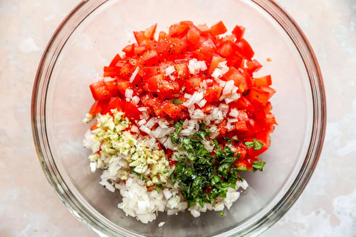 Diced tomatoes, basil, garlic, and shallots in a glass mixing bowl.