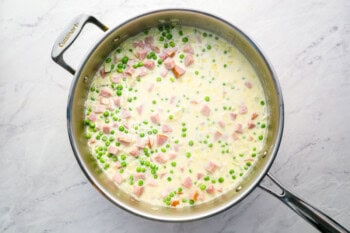 creamy sauce with peas and ham in a pan.