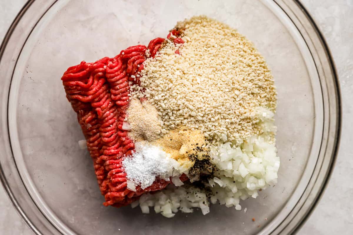 ground beef, breadcrumbs, onion, and seasonings in a glass bowl.