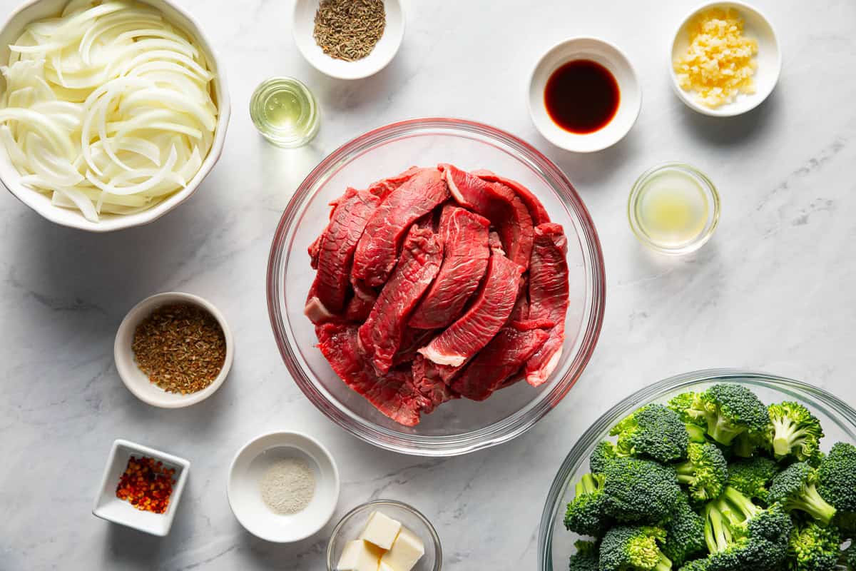 Steak and broccoli ingredients arranged in small bowls on a countertop.