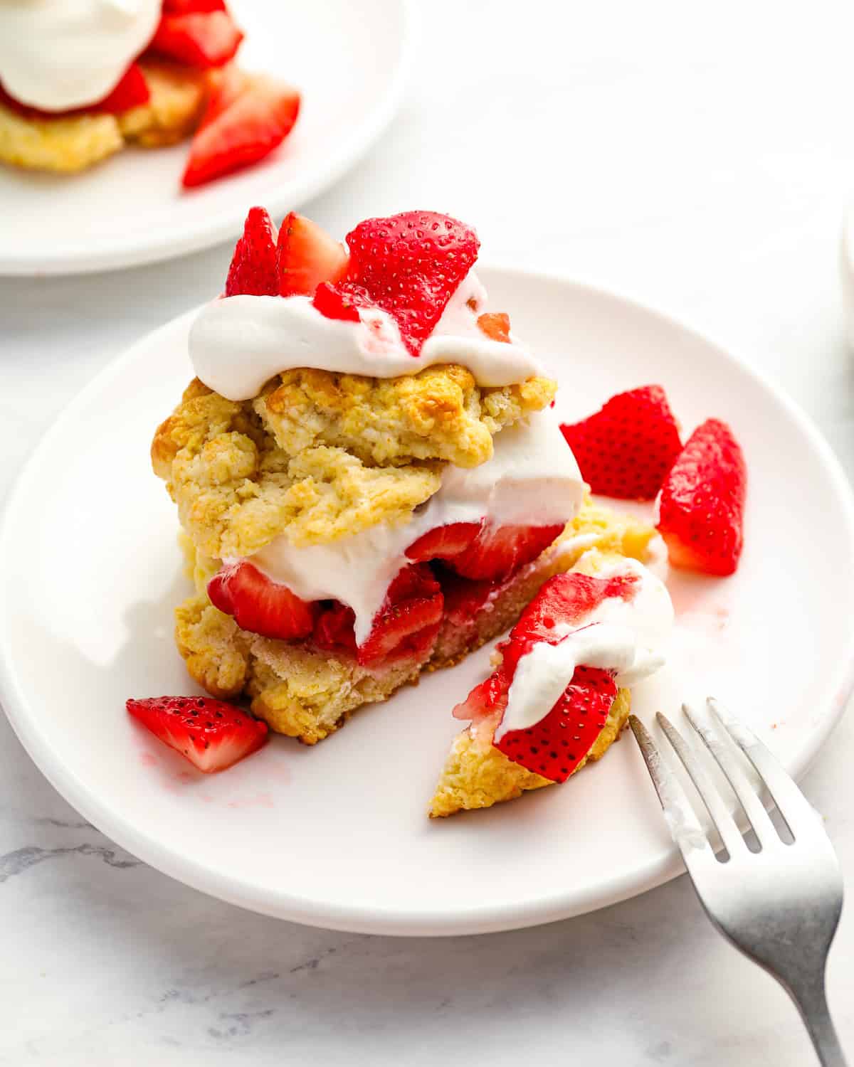 cut strawberry shortcake on a white plate with a fork.