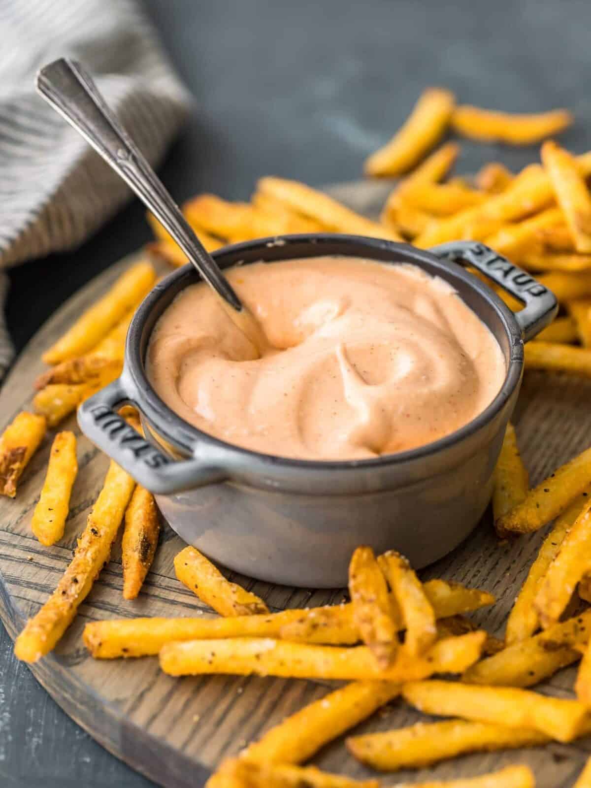 A wooden cutting board displaying a bowl of ketchup and french fries, commonly known as fry sauce.