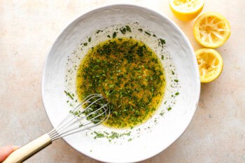 whisking herby dressing in a white bowl.