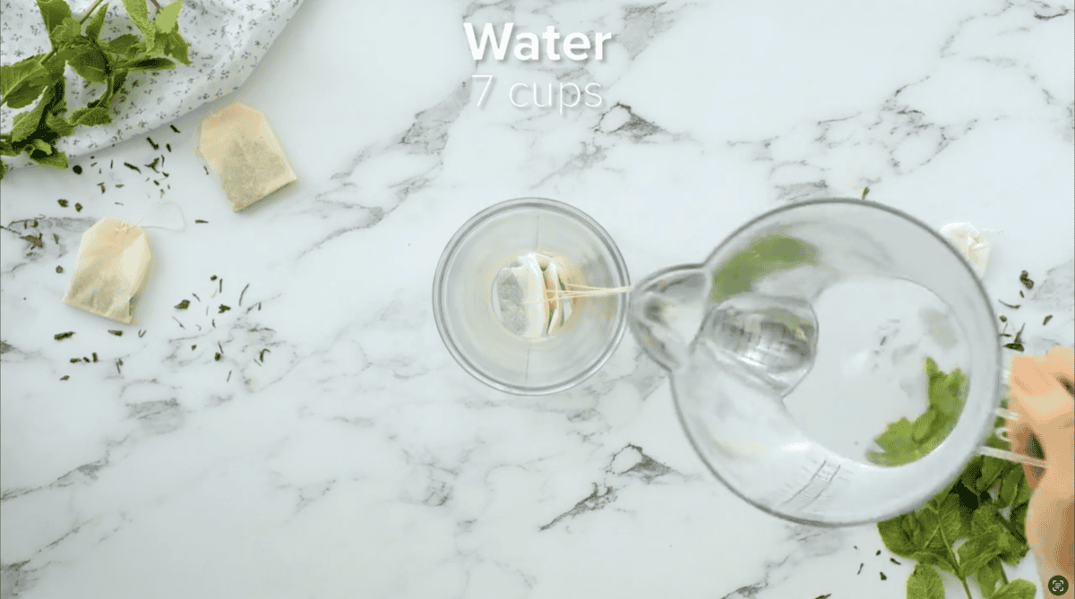 Pouring 7 cups of water into a pitcher filled with tea bags.