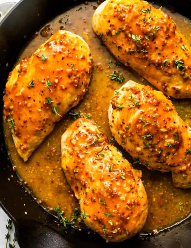 overhead view of 4 honey mustard chicken breasts in a cast iron skillet.