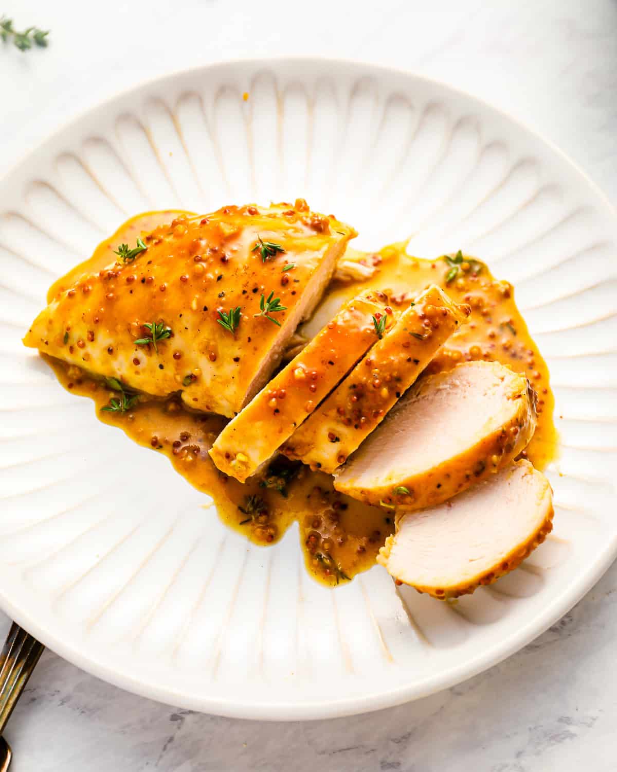 a sliced honey mustard chicken breast on a white plate.