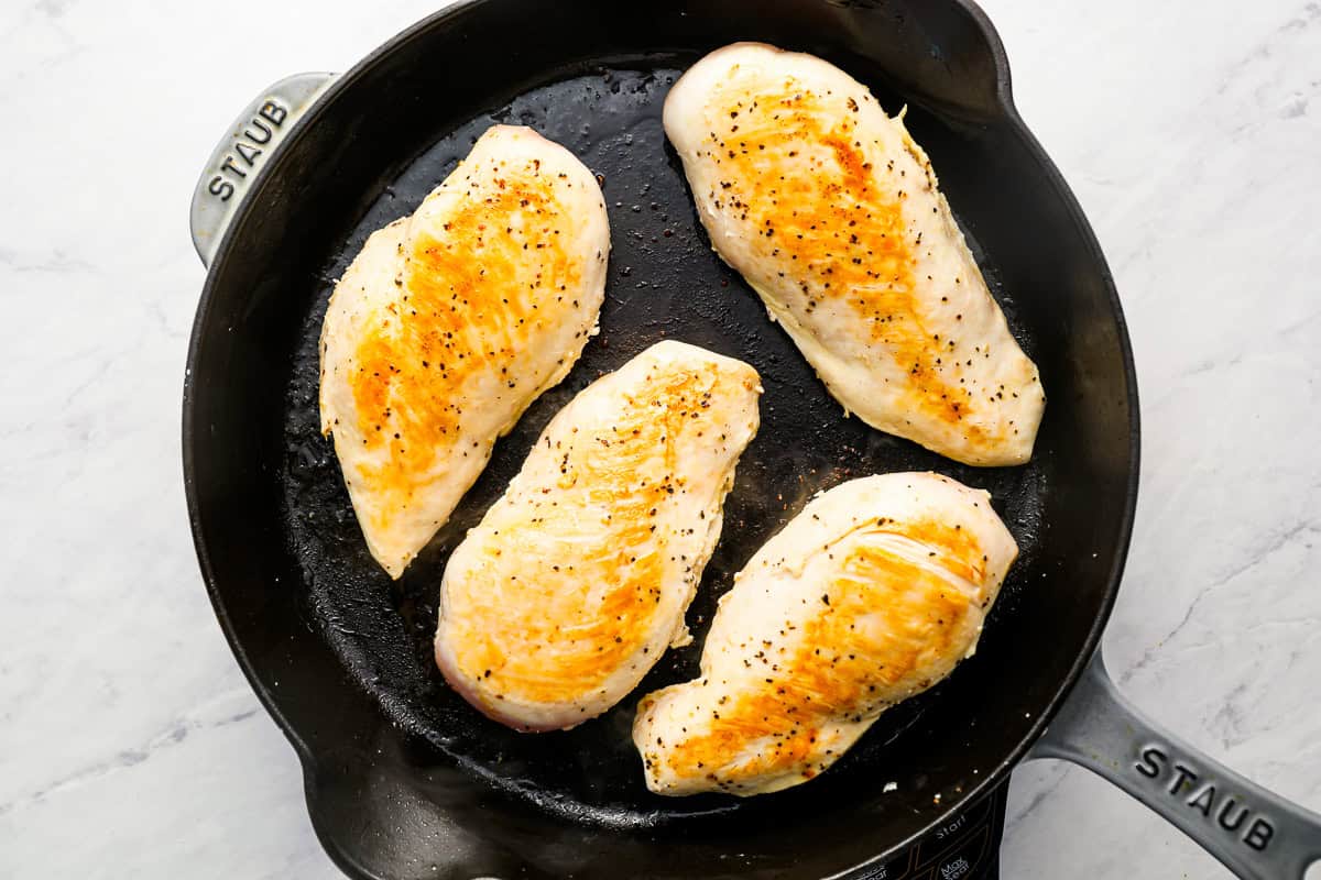 4 seared chicken breasts in a cast iron skillet.