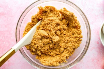 crumbly graham cracker crust in a glass bowl with a rubber spatula.