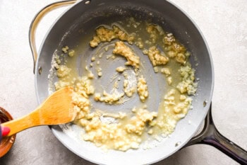 flour-coated onions in a pan with a wooden spoon.