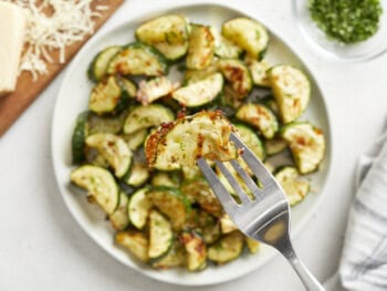 a fork stabbing a slice of roasted zucchini from a plate.