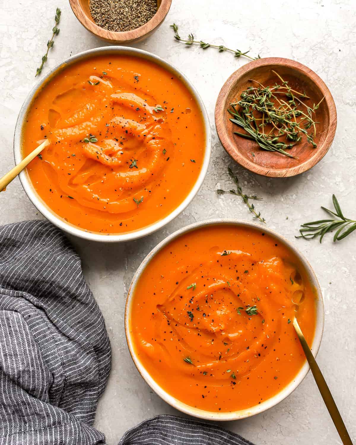 overhead view of bowls of butternut squash soup with spoons and herbs.