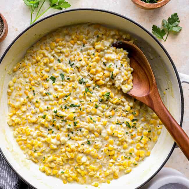 overhead view of creamed corn in a dutch oven with a wooden spoon.