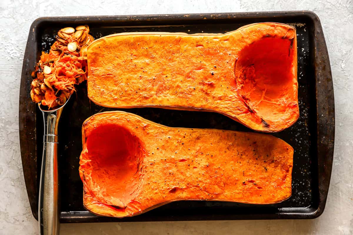 roasted and seeded halves of a butternut squash on a baking sheet.