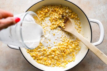 pouring milk/flour slurry into creamed corn in a dutch oven with a wooden spoon.