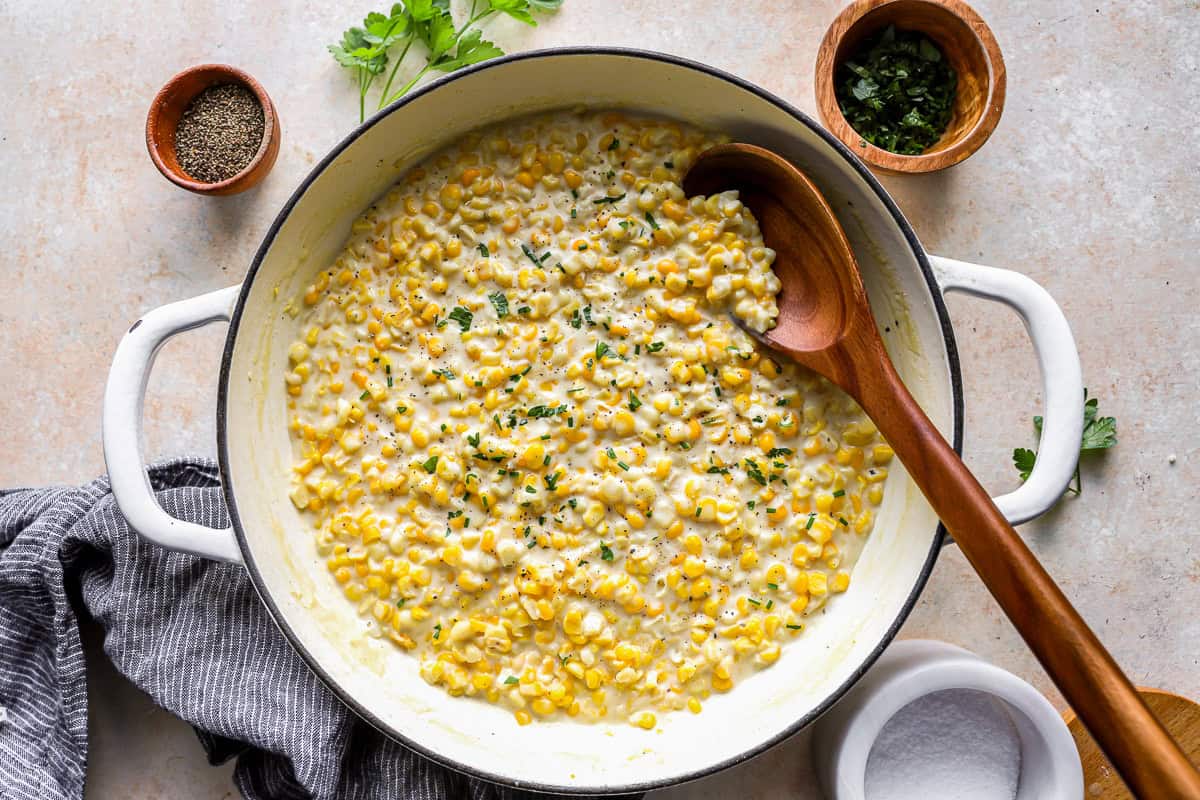 overhead view of creamed corn in a dutch oven with a wooden spoon.