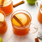 a glass of apple cider topped with an apple slice and a cinnamon stick.