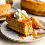 a partially eaten slice of pumpkin cheesecake on a plate with caramel sauce, whipped cream, and a fork.