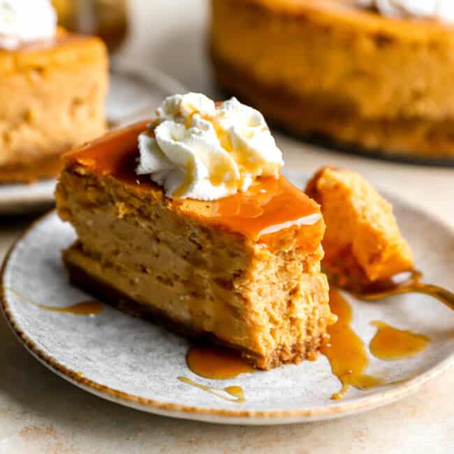 a partially eaten slice of pumpkin cheesecake on a plate with caramel sauce, whipped cream, and a fork.