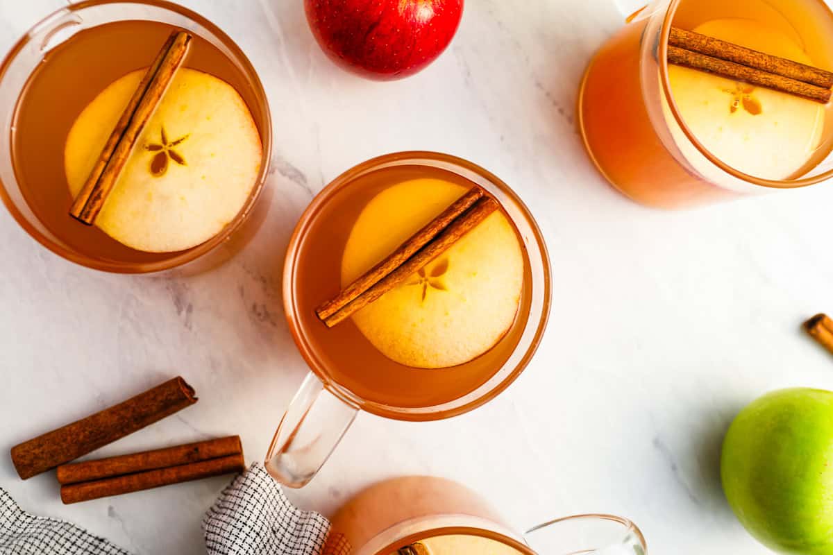 overhead view of glasses of apple cider topped with apple slices and cinnamon stick.