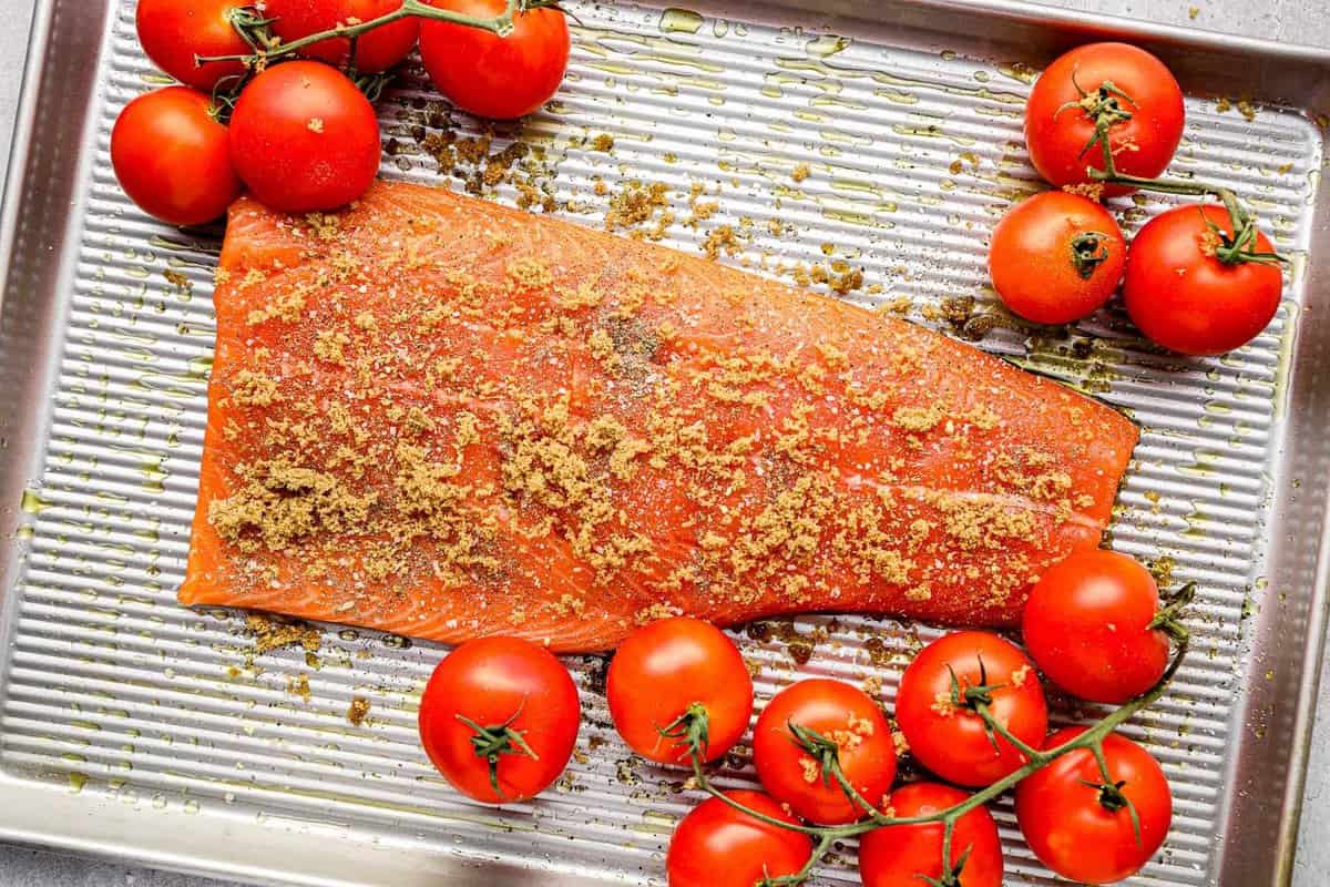 raw salmon filet on a baking tray with tomatoes on vines.