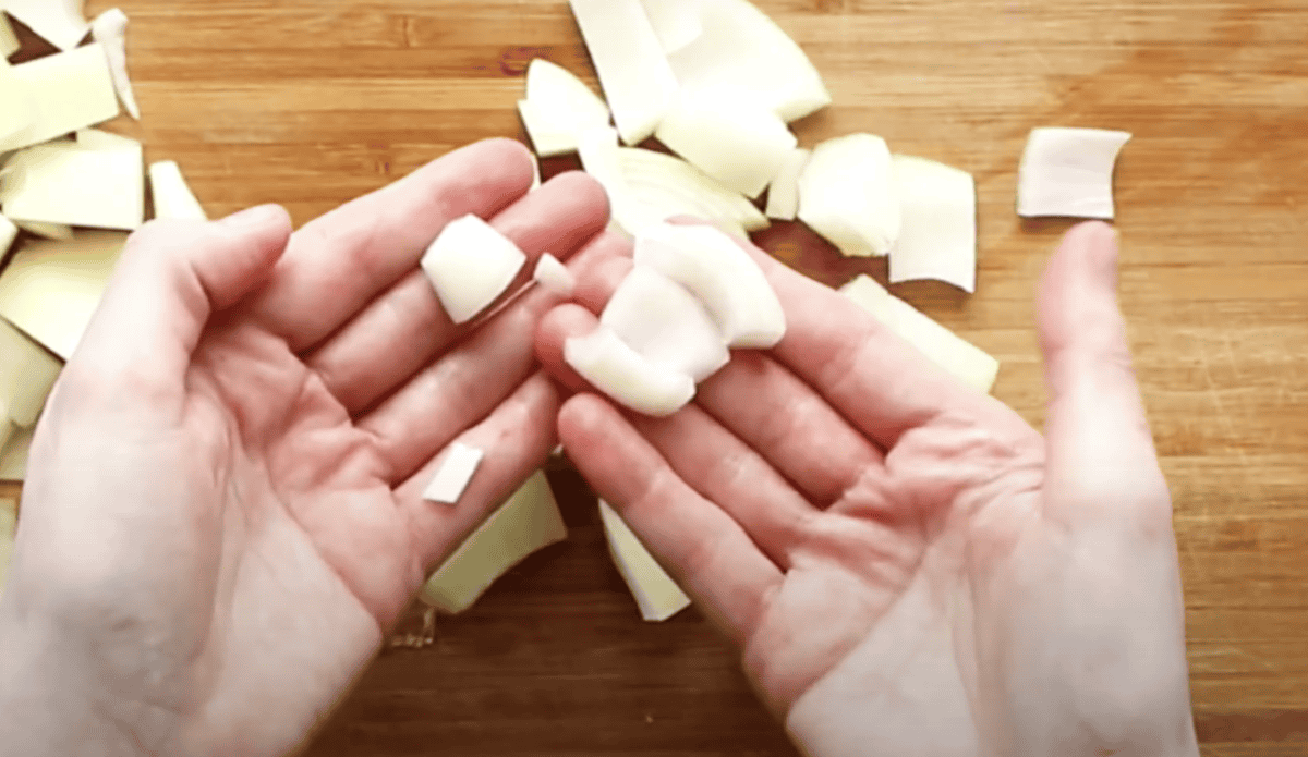 Hands holding up pieces of a chopped onion to show size.