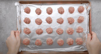 Uncooked Swedish meatballs lined up on a baking tray.