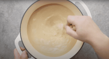 Hand whisking creamy soup in a pot.