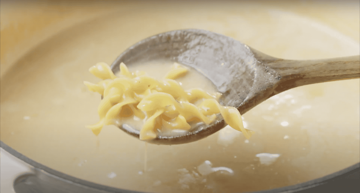 Wooden spoon lifting cooked egg noodles out of a pot of soup.