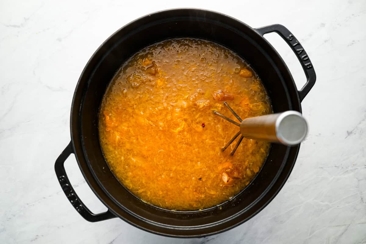 mashing cooked apples and tangerines in a pot with a potato masher.