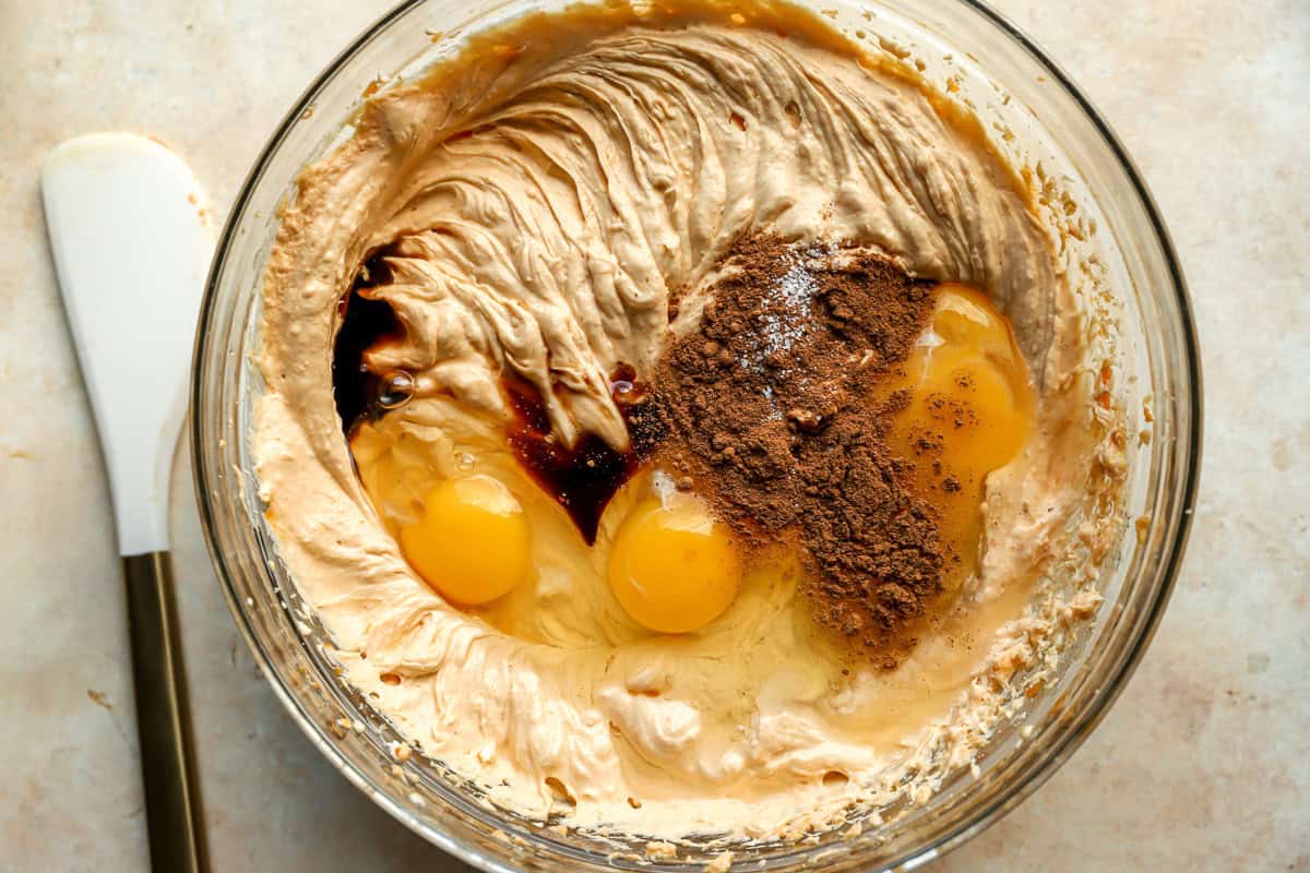 adding eggs, vanilla, and pie spice to pumpkin cheesecake batter in a glass bowl.