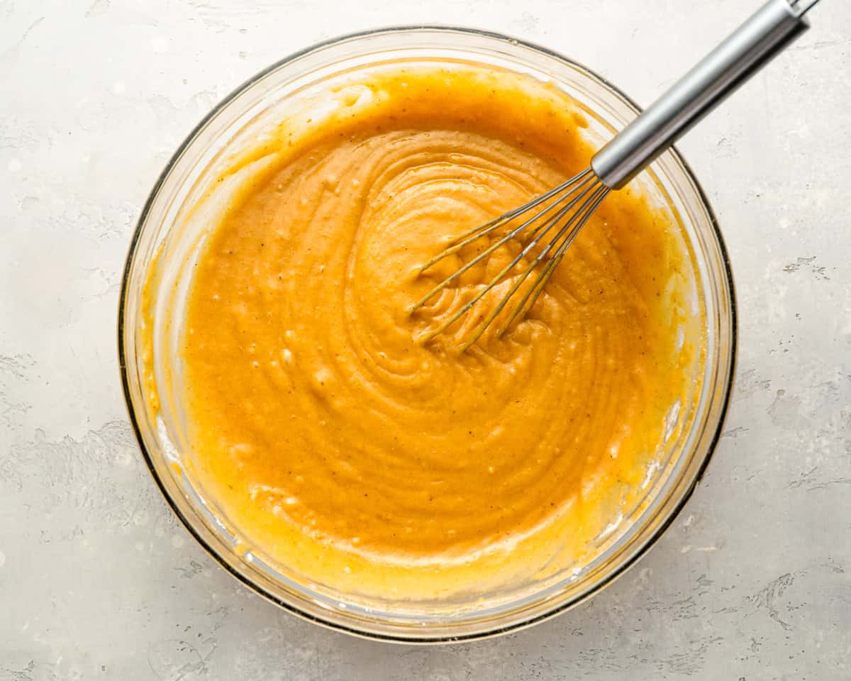 orange liquid in a glass bowl with a whisk.