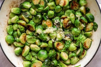 adding garlic to cooked brussels sprouts in a pan.